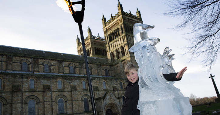 Boy smiling at camera posing with Ice sculpture and Flaming torch with Durham Cathedral in background at Fire and Ice Festival.